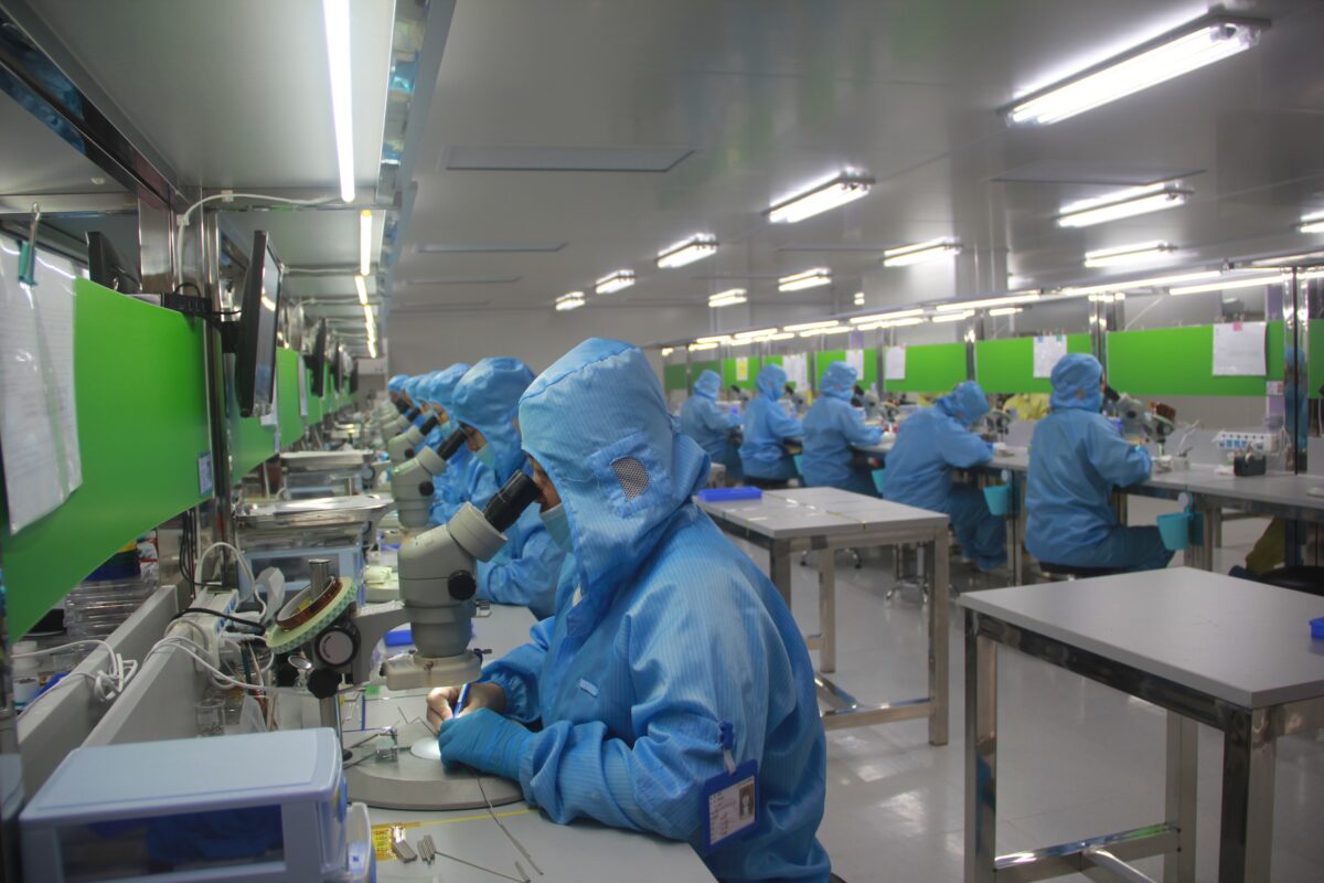 Workers in a factory in protective clothing. They look through microscopes.