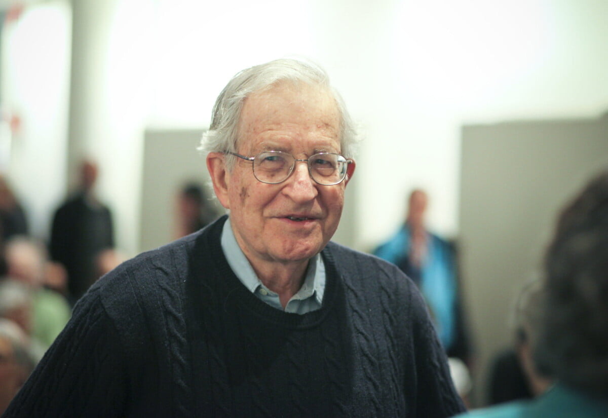 Portrait of Norman Chomsky, old male man with white hair and glasses, smiling.