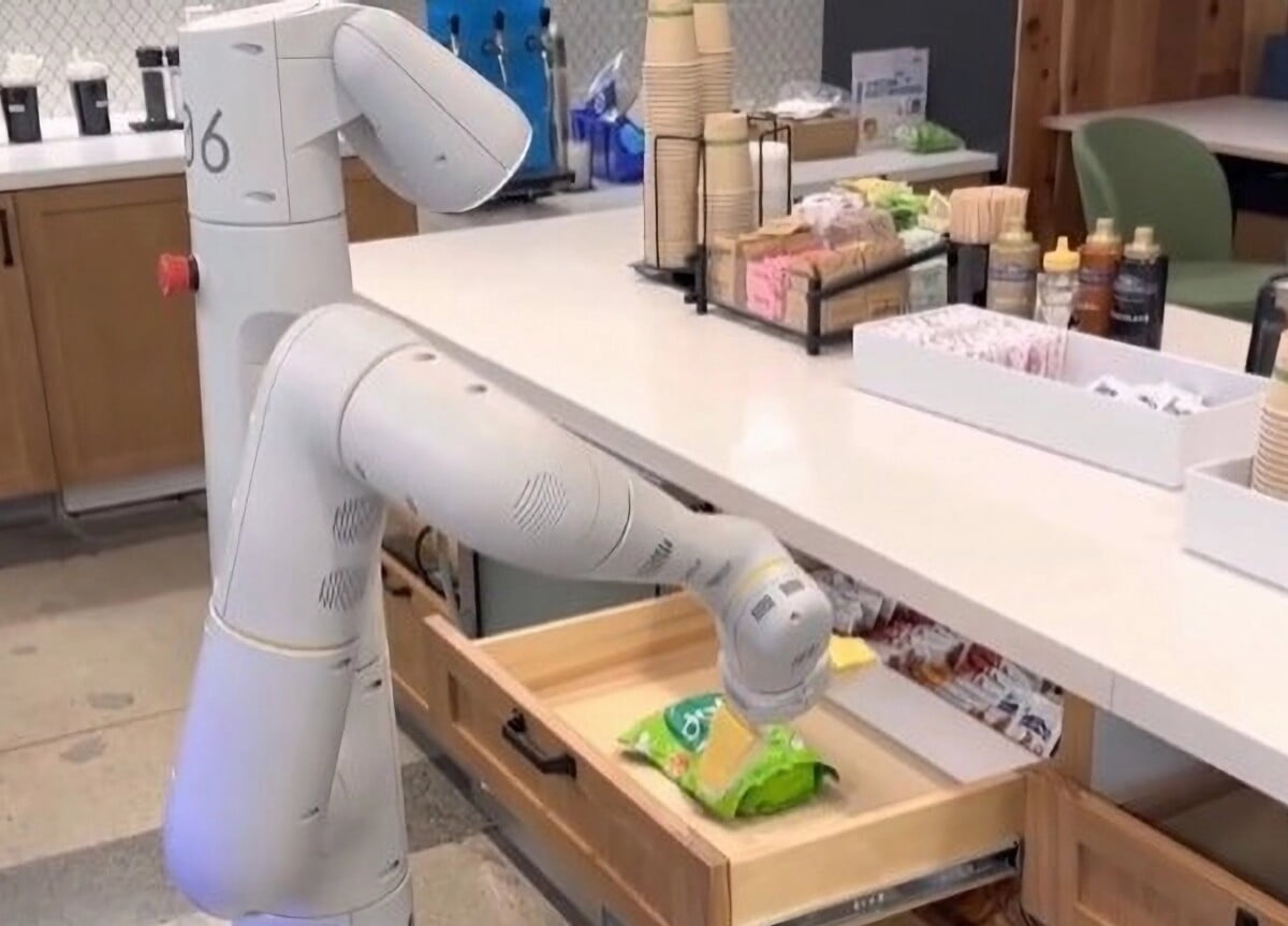A wheeled robot with a robotic arm reaches into a kitchen drawer and pulls out a bag of chips.