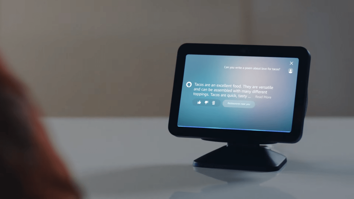 A product image of Amazon Alexa with a screen on a table. The display shows an information text about tacos.