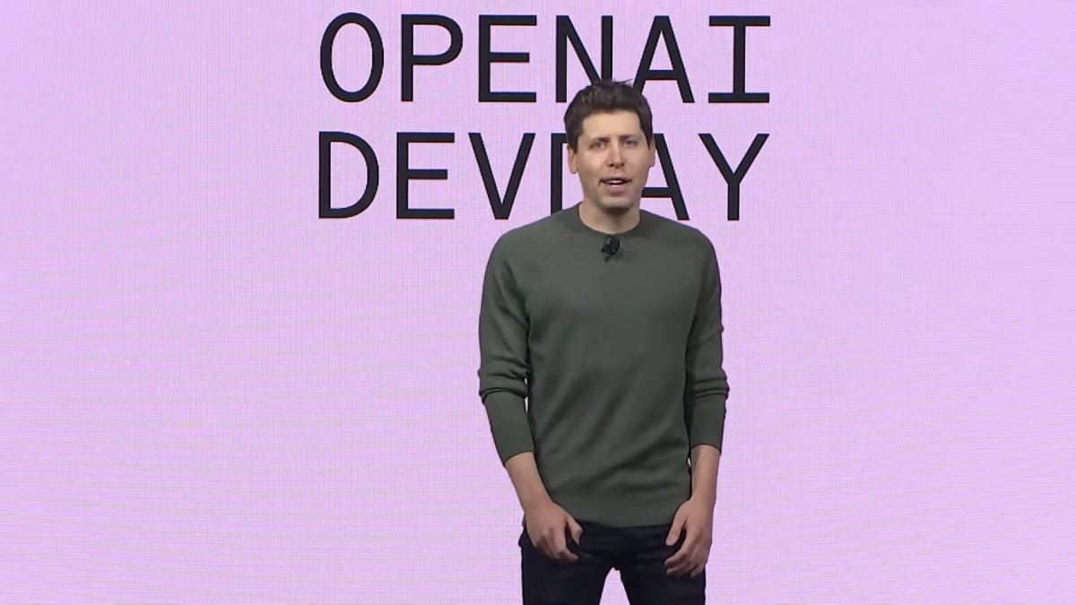 Sam Altman standing on a stage with a pink LCD screen behind him stating "OpenAI Devday"