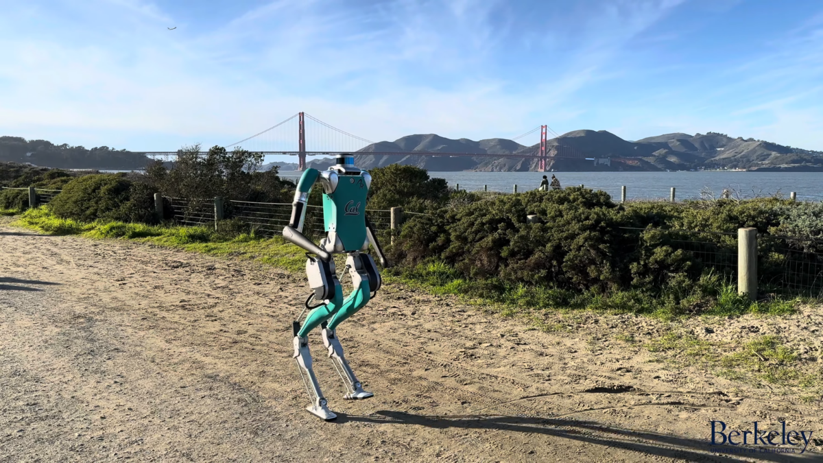 A robot walks along a sandy path, with the Golden Gate Bridge in the background.